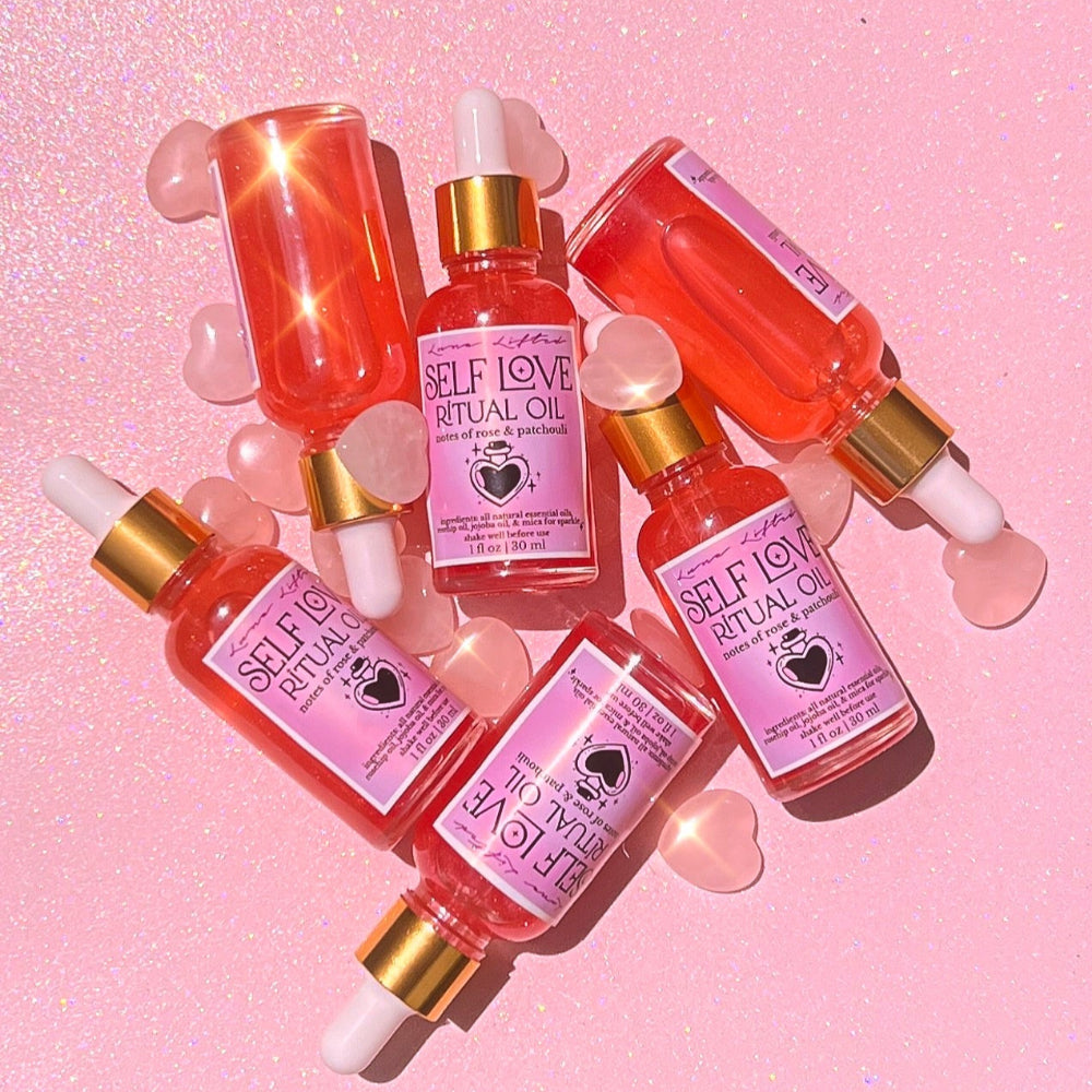 Bottles of 'Self Love Ritual Oil' on a pink background with heart shapes.