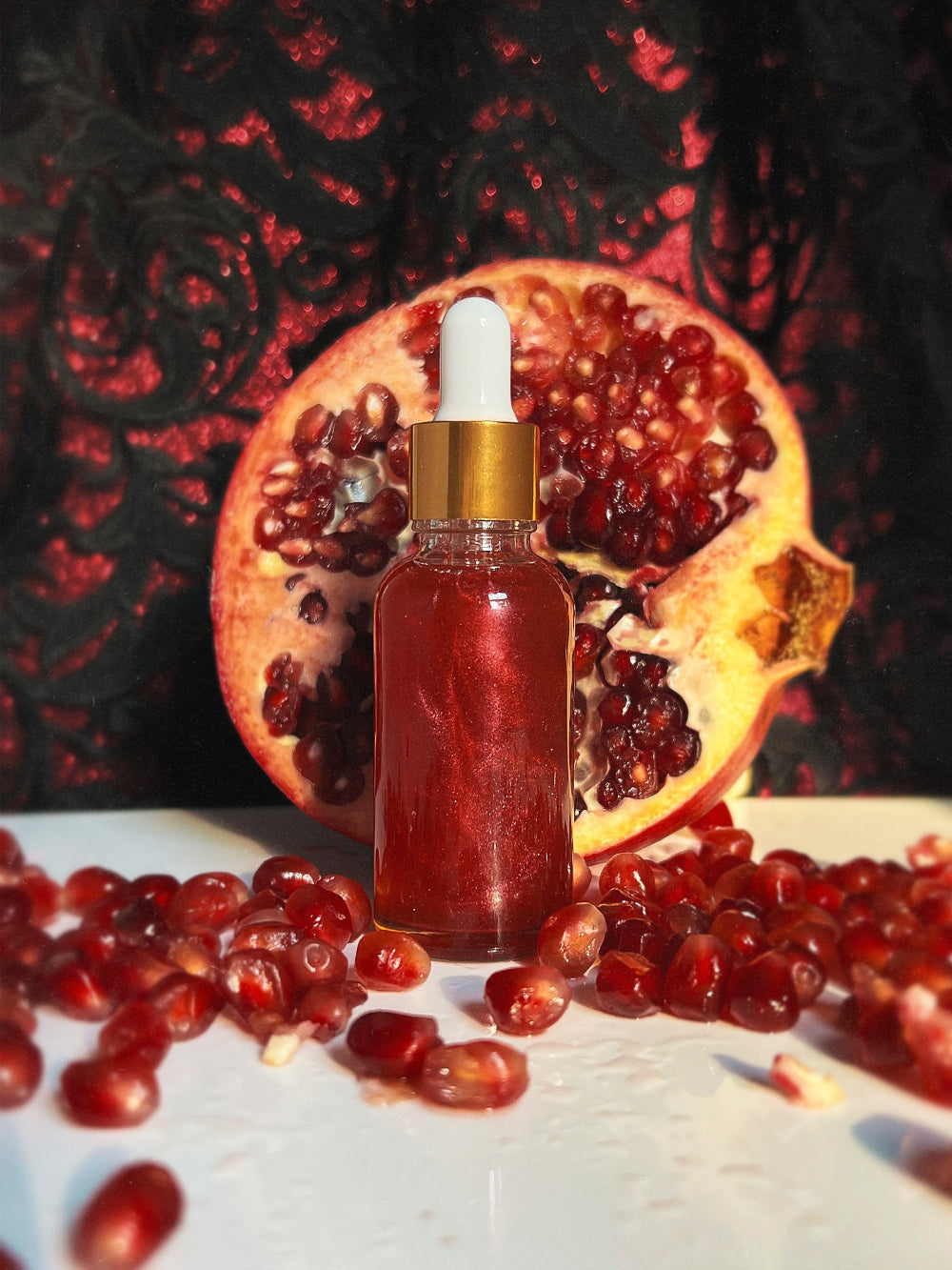 Bottle of red liquid with dropper in front of a pomegranate on a dark background