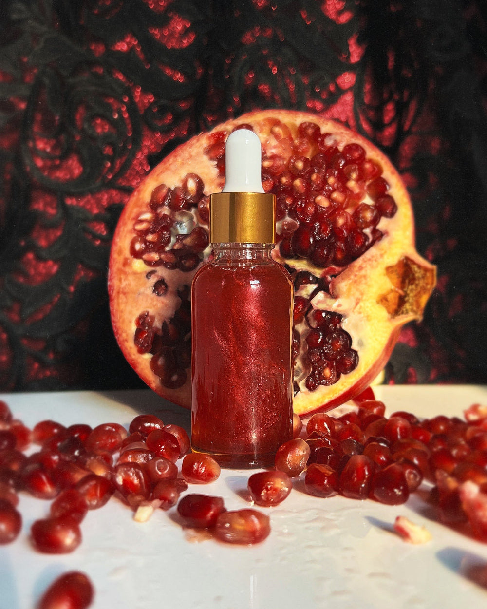 Bottle of red liquid with dropper in front of a pomegranate on a dark background