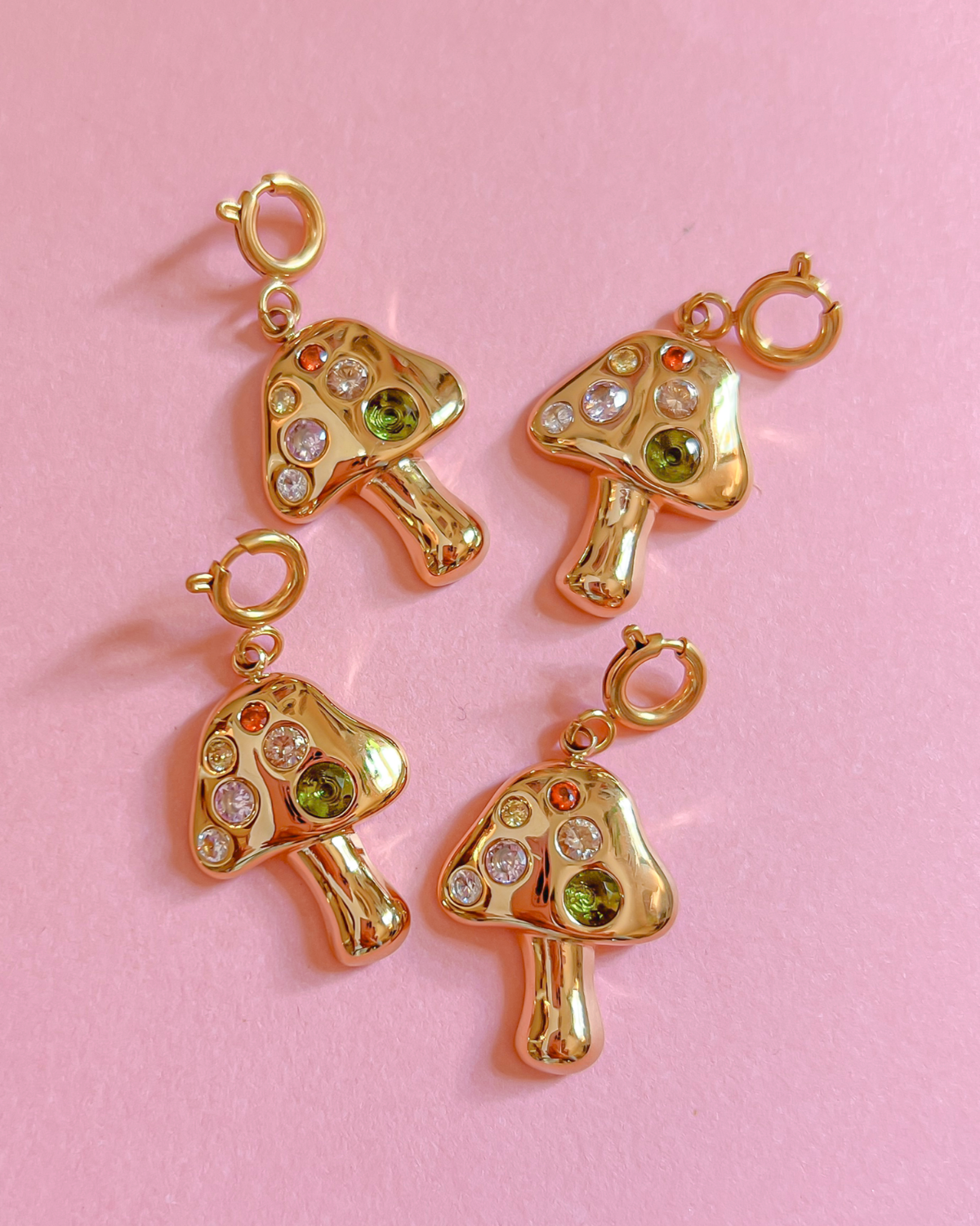 Gold mushroom-shaped charms with gemstones on a pink background